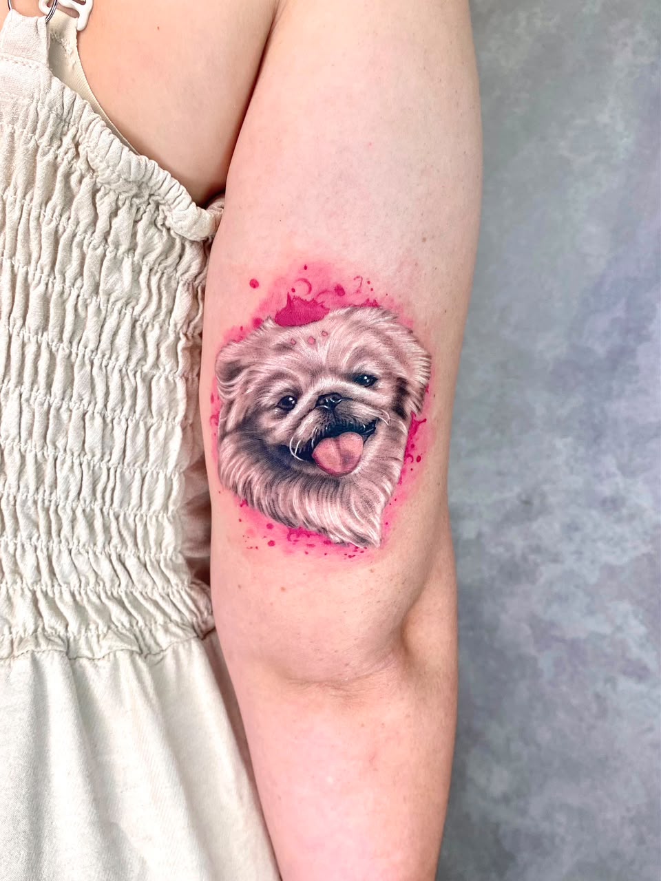 Tatuagem realista de pequinês com fundo aquarelado rosa no braço